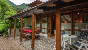 Un espace extérieur abrité, doté d’un sol en pierre, de poutres en bois et de portes vitrées donnant accès à un espace intérieur.