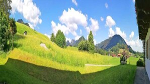 Un paysage verdoyant et luxuriant, avec un ciel dégagé, un petit bâtiment et des montagnes en arrière-plan.