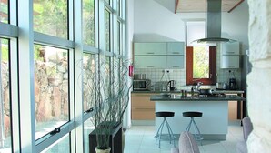 Una cocina moderna con una isla central, ventanas amplias y una zona de estar con sofá y taburetes de bar.