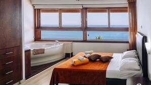 Un dormitorio con una cama, una bañera y un ventanal con vistas al mar.