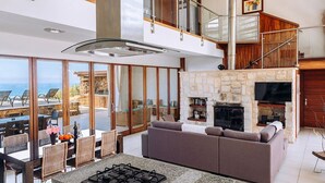 Amplia sala de estar con chimenea de piedra, cocina con estufa a gas y balcón con vistas al mar.