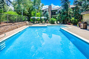 Relax by the serene pool surrounded by lush greenery and a brick wall, with lounge chairs and umbrellas for shaded seating.