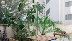 A wooden table and bench set in a courtyard with potted plants and a building in the background. - Modern Minimalist 3BD Apartment in Hilton District (Athens)