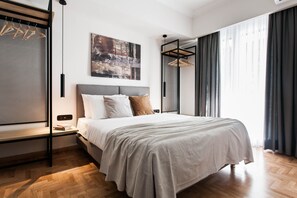 A modern bedroom with a bed, a hanging light, a painting, and a window with curtains.