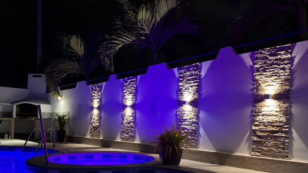 A swimming pool with a stone wall and palm trees, illuminated by blue lighting. - Large private villa with a pool and jacuzzi, close to the beach (Playas Villamil)