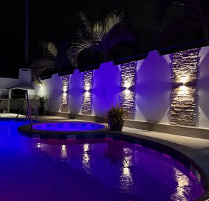 A swimming pool with a stone wall and palm trees, illuminated by blue lighting. - Large private villa with a pool and jacuzzi, close to the beach (Playas Villamil)