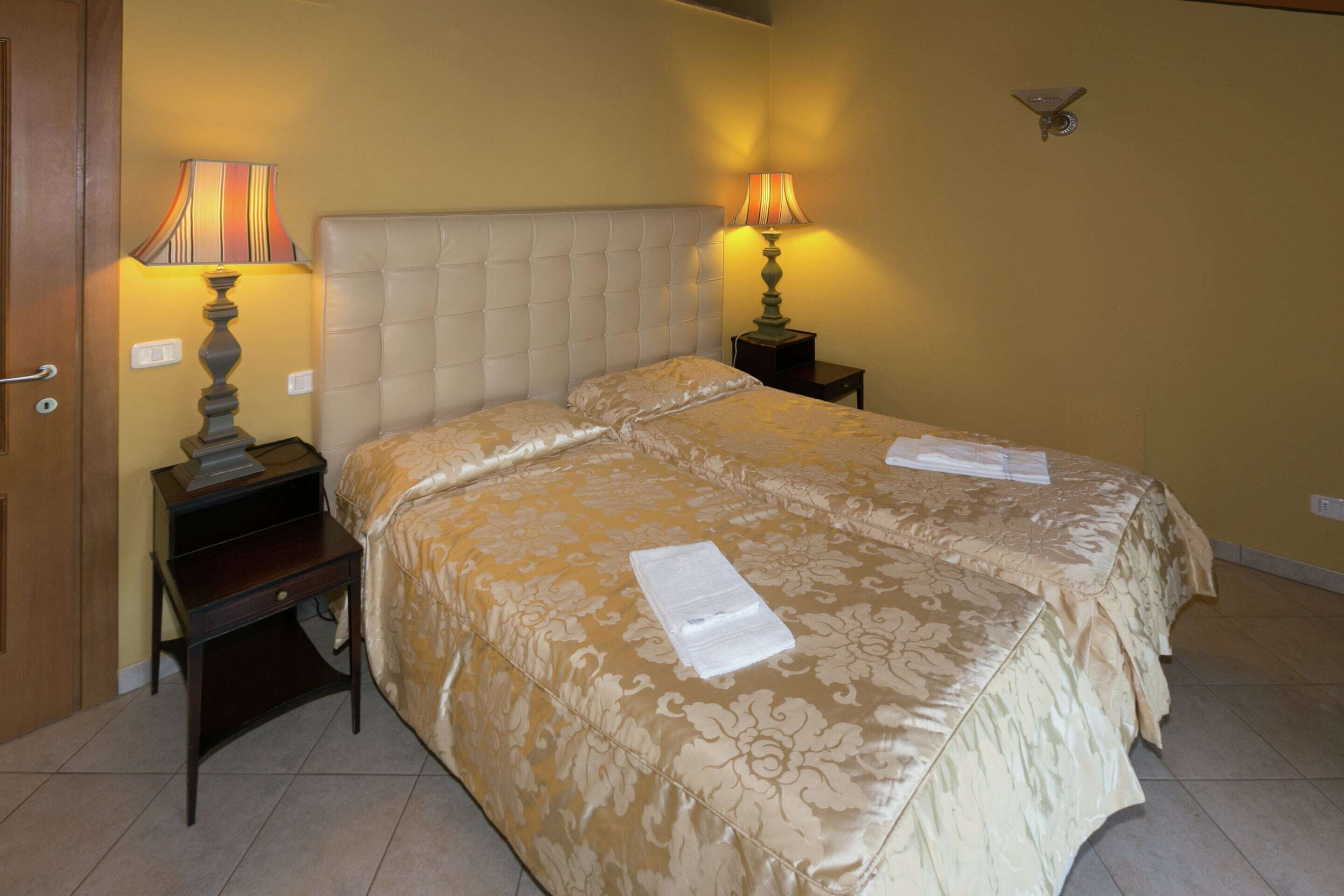 A double bed with a tufted headboard, two bedside tables with lamps, and a wall-mounted light fixture.