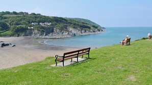 A coastal landscape with a bench overlooking the sea, grassy terrain, and a distant view of houses on a hill. - 2 bedroom accommodation in Llechryd, near Cardigan (Llechryd, near Cardigan)