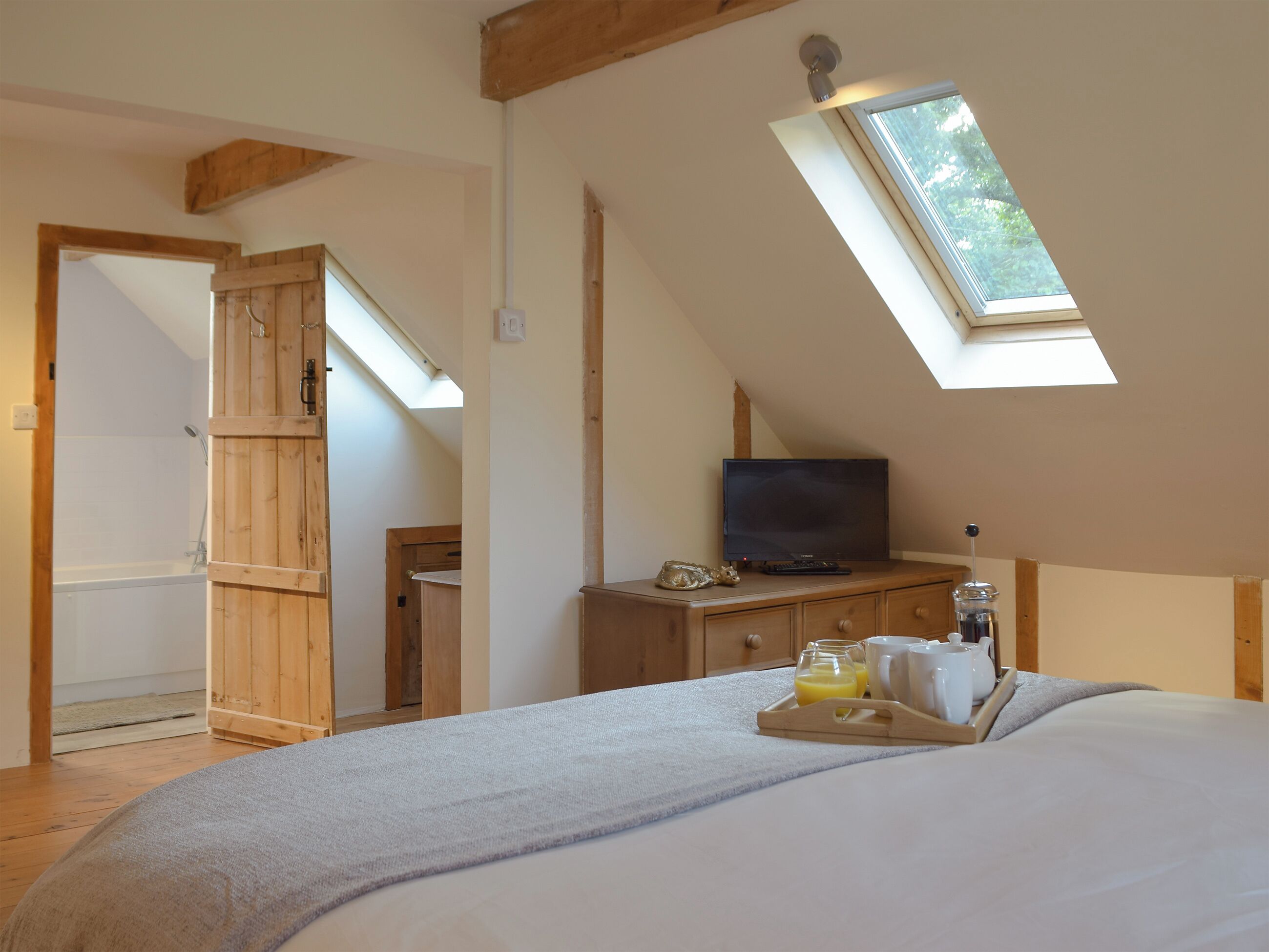 Une chambre avec un puits de lumière, un téléviseur posé sur une commode en bois et un plateau contenant des éléments pour le petit-déjeuner.