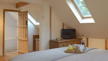 A bedroom with a skylight, a television on a wooden dresser, and a tray with breakfast items.
