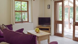 A room with a purple sofa, a television on a wooden stand, a window with a view of greenery, and a door leading outside. - 2 bedroom accommodation in Llechryd, near Cardigan (Llechryd, near Cardigan)