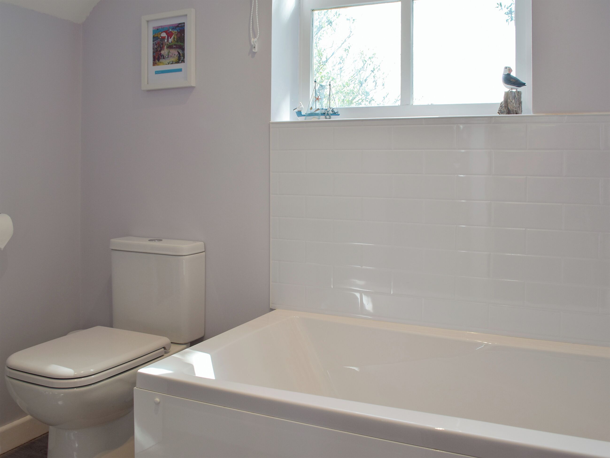 A bathroom with a toilet, a bathtub, and a window with a view of trees.