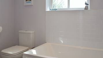 A bathroom with a toilet, a bathtub, and a window with a view of trees.