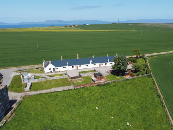 A large, white building with a blue roof, surrounded by green fields and a body of water in the background.
