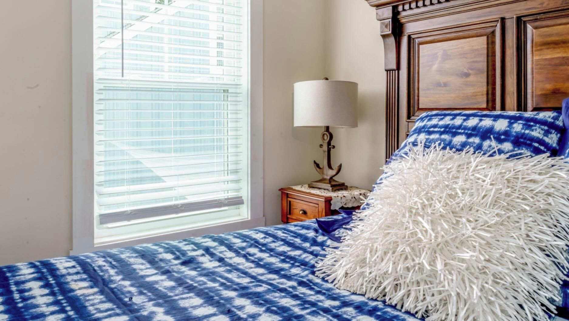 A bedroom with a bed, a nightstand, a lamp, and a window with blinds.