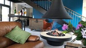 Een moderne woonkamer met een leren bank, een ronde salontafel met vuurhaard, een eethoek met bar, en een trap met blauwe wanden.
