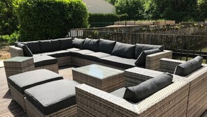 Een modulaire buitenbank met kussens, een salontafel met glazen blad en een houten terras.