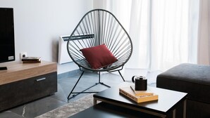 Una sala de estar moderna con una butaca de alambre curvada, un televisor de pantalla plana, una mesa de centro con libros y un sofá gris.