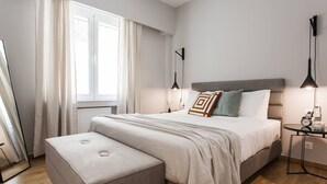 A modern bedroom with a large bed, a bedside table, a nightstand, a mirror, and a window with curtains. - Peaceful 2BD Apartment in Kolonaki (Athens)
