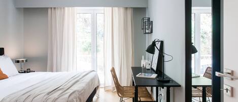 A bedroom with a bed, a desk, and a chair. There is a window with curtains and an air conditioning unit above the window.