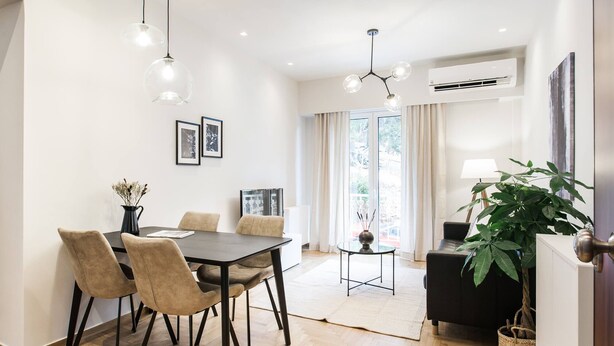 A modern dining area with a wooden table, cushioned chairs, and pendant lighting. - Peaceful 2BD Apartment in Kolonaki (Athens)