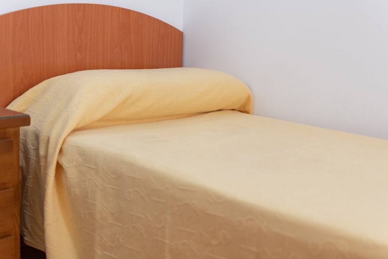 Ein Einzelbett mit Holz-Kopfstück und einer beige farbenen Bettdecke.