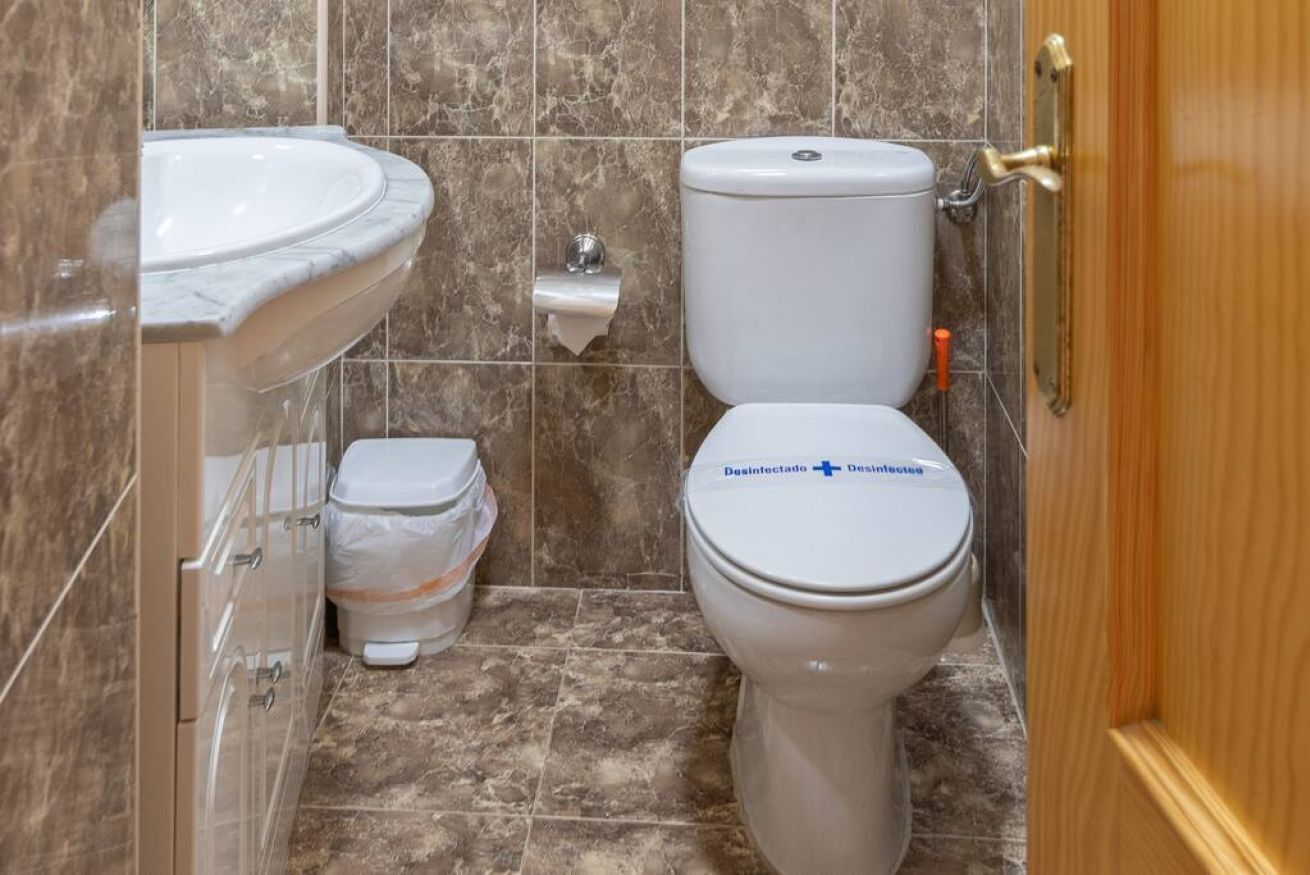 A bathroom with a white toilet, a sink, and a trash bin.