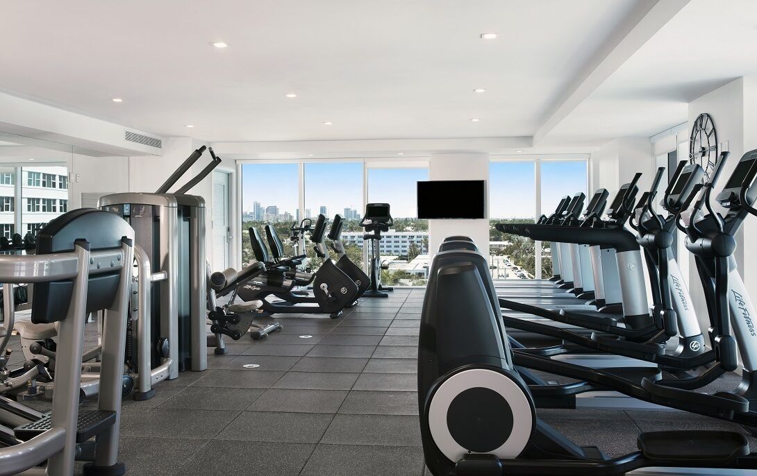 A gym with cardio machines, weight equipment, and a large window offering a city view.