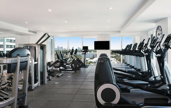 Une salle de sport équipée de machines de cardio, de matériel de musculation et dotée d’une grande fenêtre donnant sur la ville.