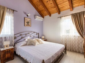 A bedroom with a wooden ceiling, a bed with a white bedspread, two bedside tables with lamps, and a wall-mounted air conditioner. - Luxurious Villa in Selca With Pool (Selca)