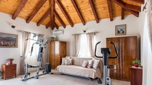 Una habitación con techo de madera inclinado, una cama, equipo de ejercicio, un sofá y un armario.