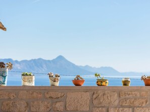 Pared de piedra con plantas en macetas y vistas a montañas y agua.