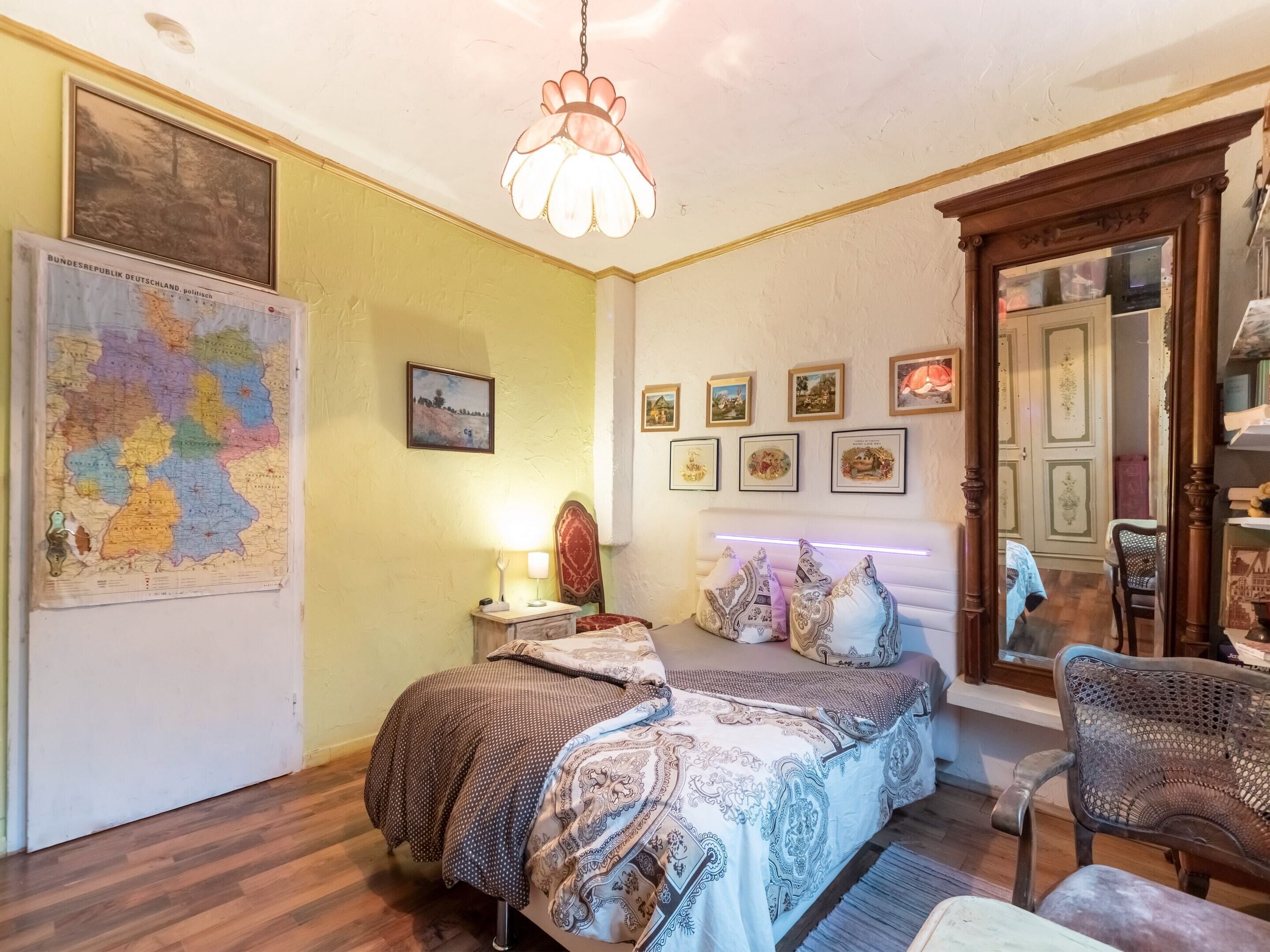 Un dormitorio con una cama, una silla, un mapa y varias fotografías enmarcadas en la pared.