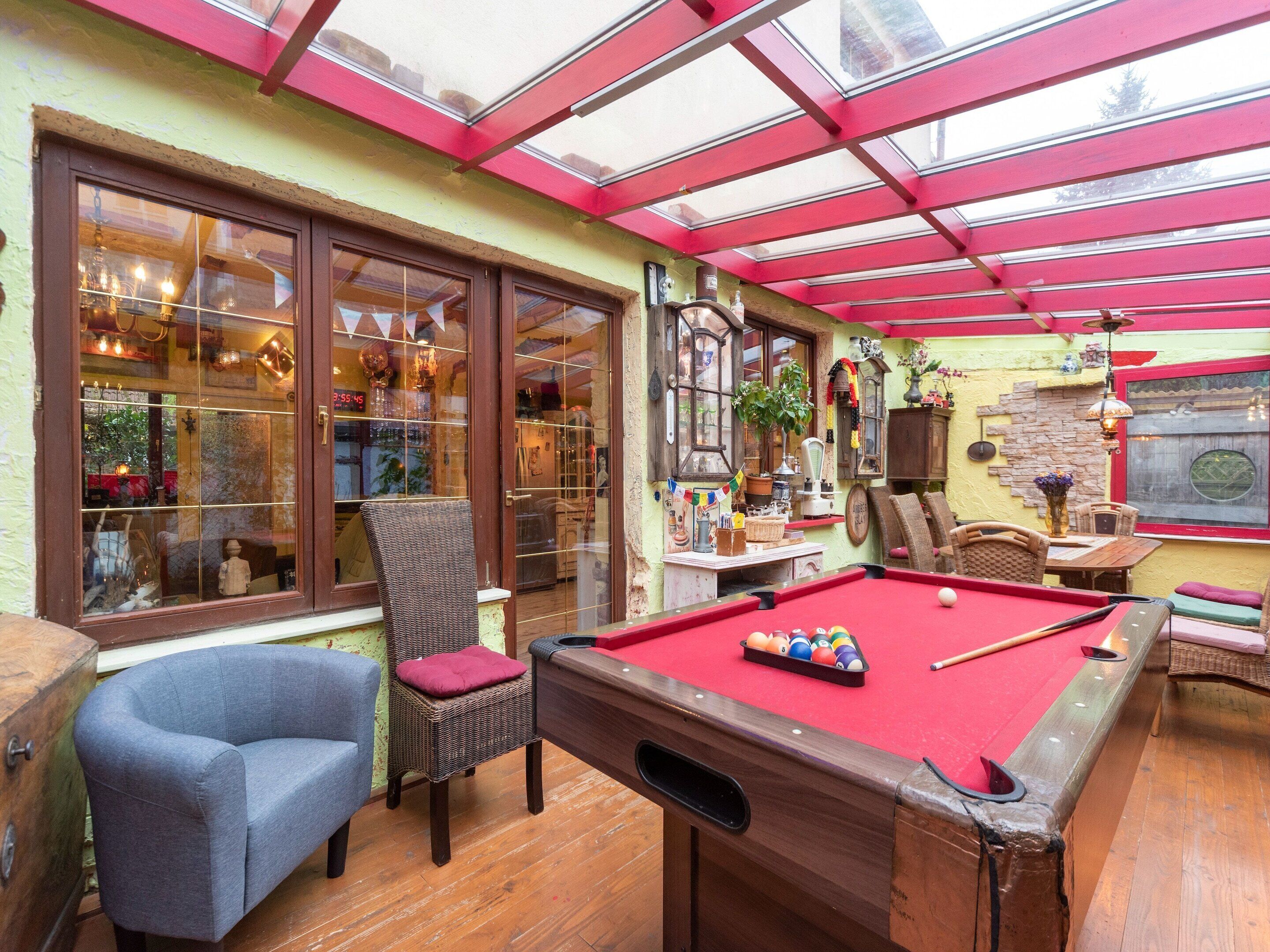 A cozy indoor pool area with a wooden pool table, comfortable seating, and a glass-enclosed patio.