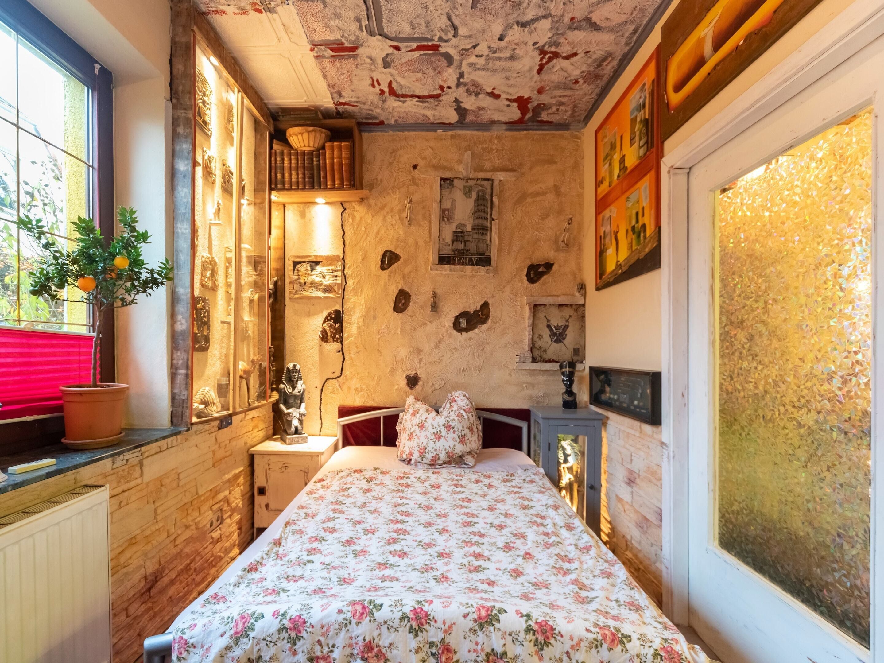 A bedroom with a bed, a nightstand, a window with a view, and a potted plant.