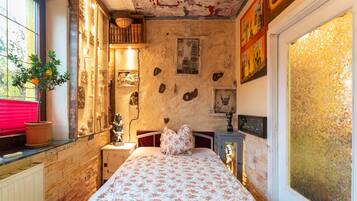 A bedroom with a bed, a nightstand, a window with a view, and a potted plant.