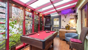 Una mesa de billar en una sala con techo de cristal, un dardo y una silla.