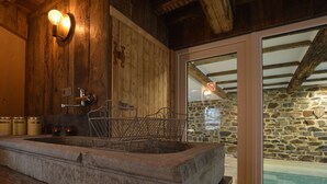 A stone basin with metal chairs, wooden walls, a stone wall, and a glass door leading to a pool. - Country Home in Theux With Pool & Sauna (Theux)
