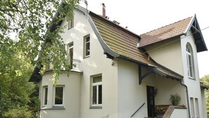 A two-story house with a sloped roof, a front porch, and a small garden area. - Villa With Garden on the Edge of the Forest (Bad Doberan)