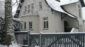 A snow-covered house with a dark wooden fence, a balcony, and a chimney. - Villa With Garden on the Edge of the Forest (Bad Doberan)