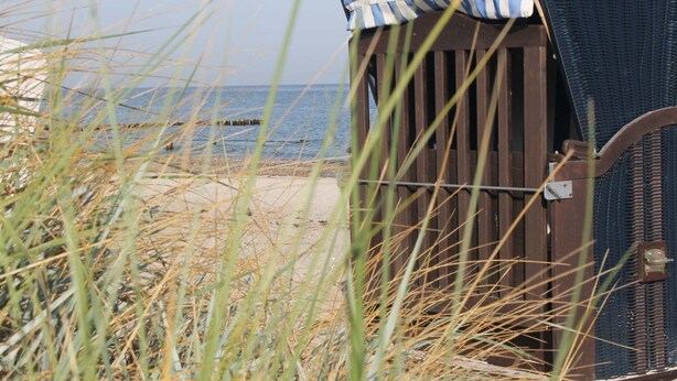 A beach hut with a striped awning, situated on a sandy beach with grass in the foreground. - Villa With Garden on the Edge of the Forest (Bad Doberan)
