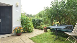 A patio area with a table and chairs, surrounded by greenery and a white building. - Villa With Garden on the Edge of the Forest (Bad Doberan)