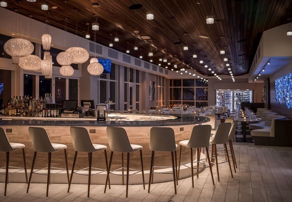 Eine moderne Bar mit einer zentralen Bar, verschiedenen Sitzgelegenheiten und einer Holzzahlendecke mit hängenden Lampen.