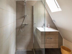 A modern bathroom with a glass shower enclosure, a white sink, and a wooden cabinet.