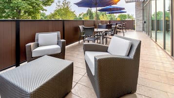 An outdoor patio area with wicker furniture, including chairs and a small table, and blue umbrellas.