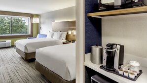 Habitación de hotel con dos camas, microondas, cafetera y una bandeja con tazas de café y cremas.