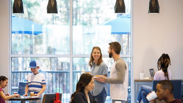 Un espacio interior moderno con ventanas amplias, mesas y sillas dispuestas para comer y conversar.