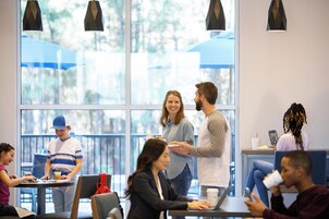 Un espacio interior moderno con ventanas amplias, mesas y sillas dispuestas para comer y conversar.