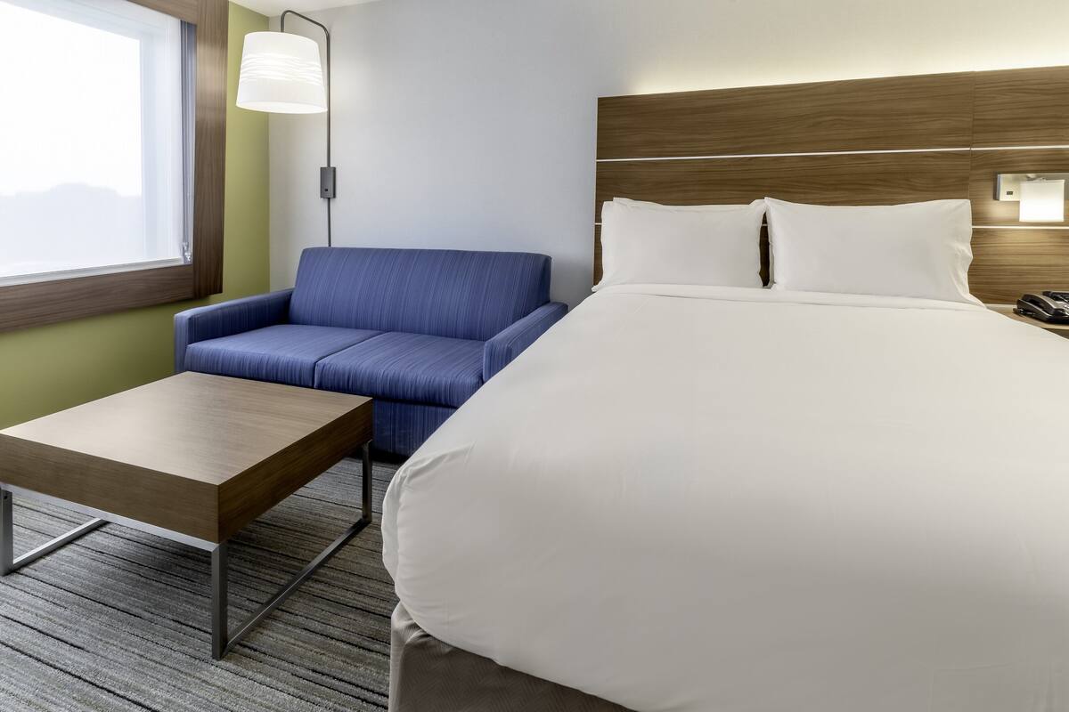 A hotel room with a bed, a blue sofa, a wooden table, and a lamp.