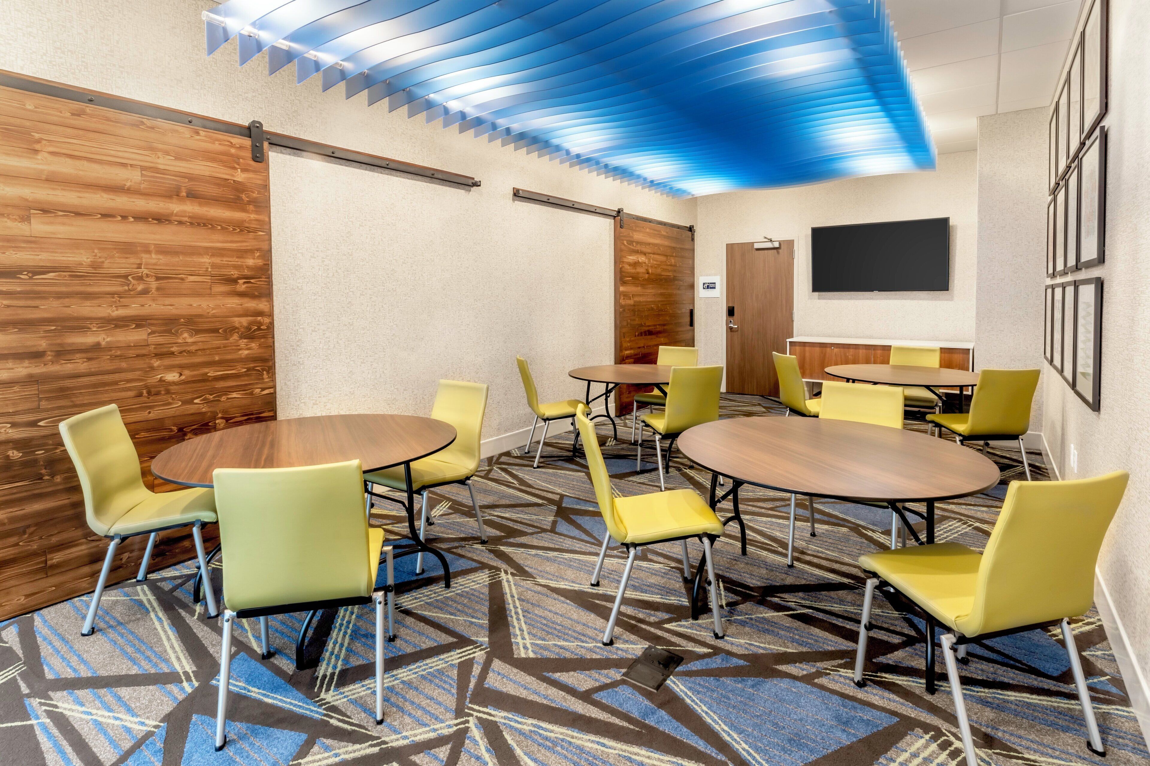 Un salón de conferencias con mesas redondas y sillas amarillas, un revestimiento de madera decorativo y una alfombra estampada.
